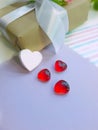 White and red hearts in front of gift box on lavender paper background.